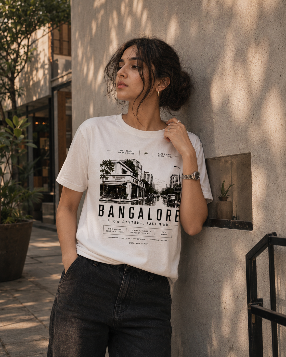 Woman wearing a white t-shirt with 'Bangalore' design leaning against a wall.