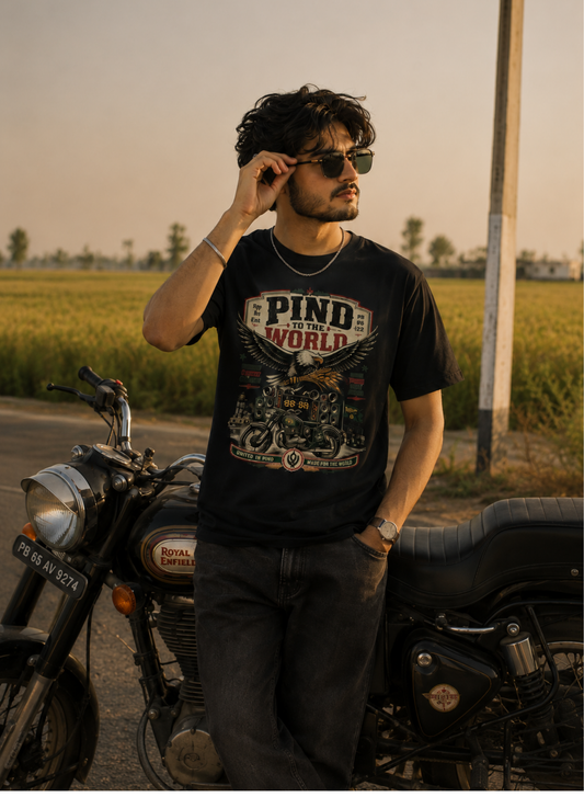 Man with a 'PIND' (Punjab) design T-Shirt standing next to a motorcycle with a scenic background